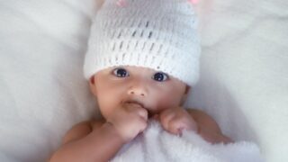 baby in white knit cap lying on white textile