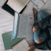 woman in blue long sleeve shirt and blue denim jeans sitting on bed using laptop