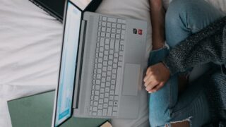 woman in blue long sleeve shirt and blue denim jeans sitting on bed using laptop