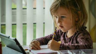 girl in purple and black long sleeve shirt holding black pen writing on white paper