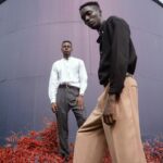 two men standing on red flower in front of gray metal wall